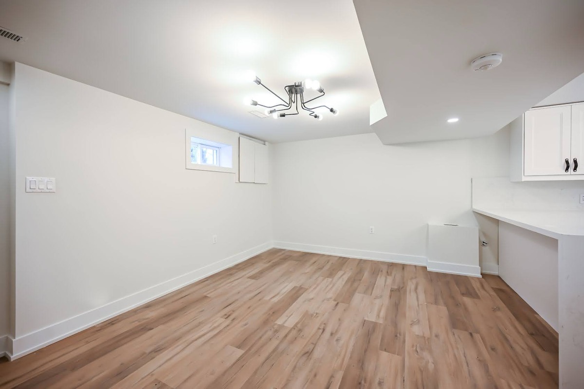 Clean finished basement with warm wood floors and modern fixtures — excellent wide-angle portfolio shot — Winchester, Hamilton | MTC Renovations