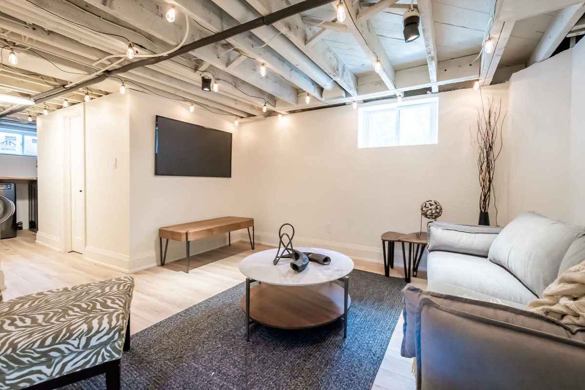 Beautifully finished basement with exposed beam ceiling, professional staging, and warm lighting — premium portfolio shot — Rosedene, Hamilton | MTC Renovations
